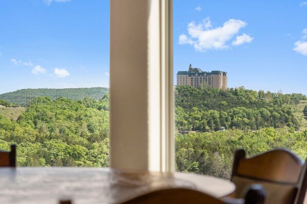 A view from a window overlooking a lush green landscape with a large building on a hill.