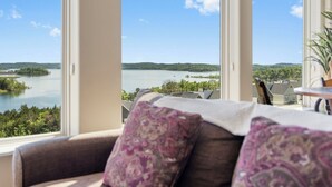 Ein Zimmer mit großem Fenster und Blick auf einen See sowie bewaldete Hügel.