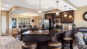 Une cuisine moderne dotée d’un îlot central, de meubles en bois foncé, d’appareils électroménagers en acier inoxydable et de luminaires suspendus.