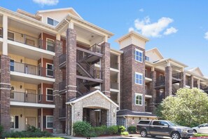 A multi-story apartment building with balconies, brick and stone exterior, and a small entrance with a covered porch. - Lakeview Escape • Modern 2BR/2BA w/ Sunroom, Jetted Tub + Pool (Branson)