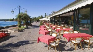 A seaside restaurant with outdoor seating, tables covered with red tablecloths, wicker chairs, and a view of the sea. - Du Lac Hotel (Sirmione)