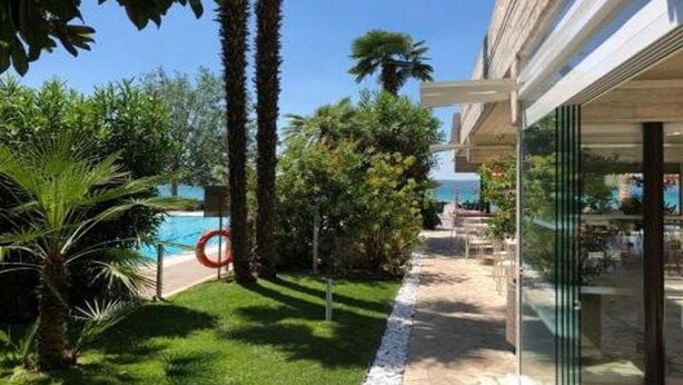 A modern building with a glass facade, a pool, and lush greenery. - Du Lac Hotel (Sirmione)