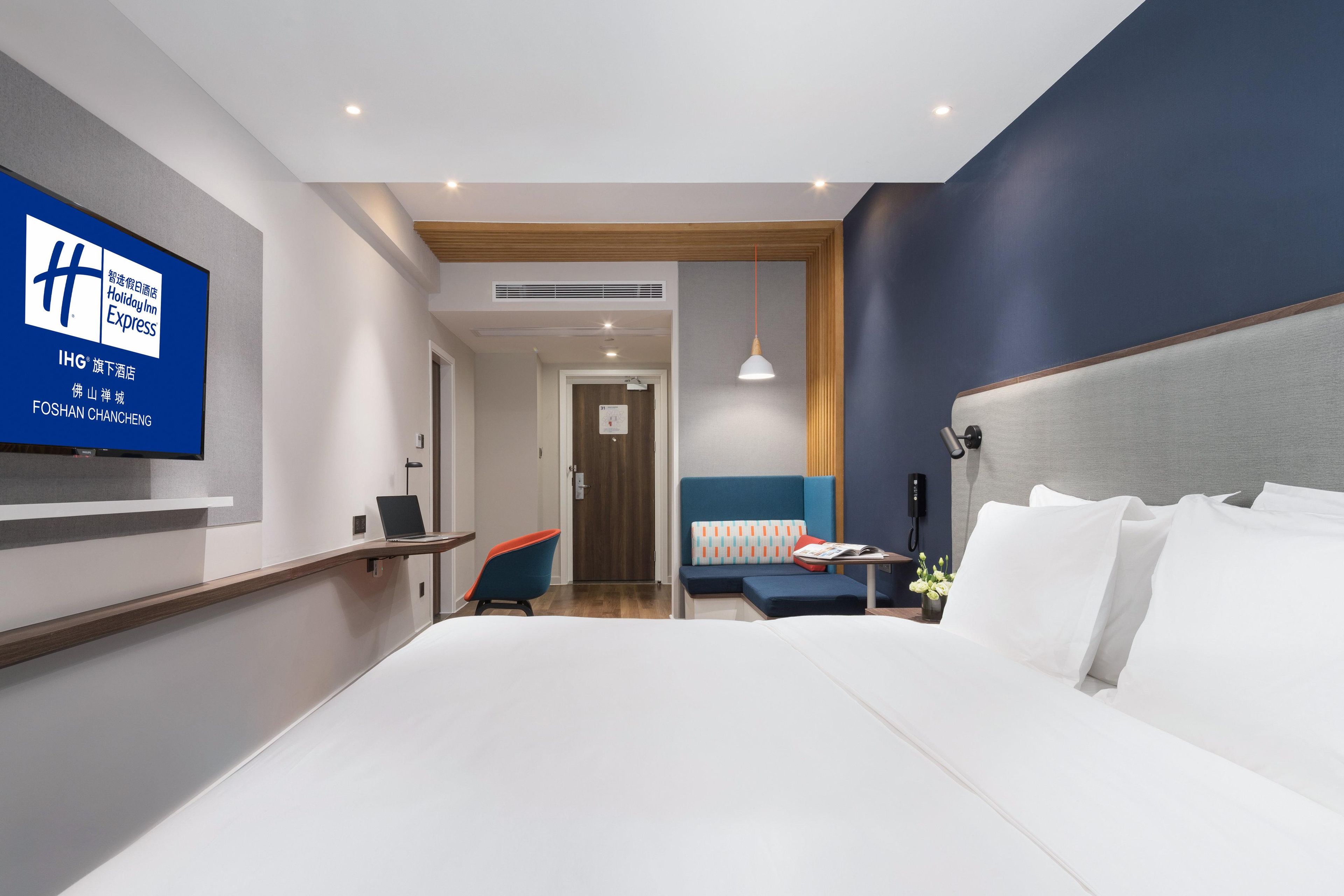 A hotel room with a large bed, a desk, a chair, a TV, and a sofa.