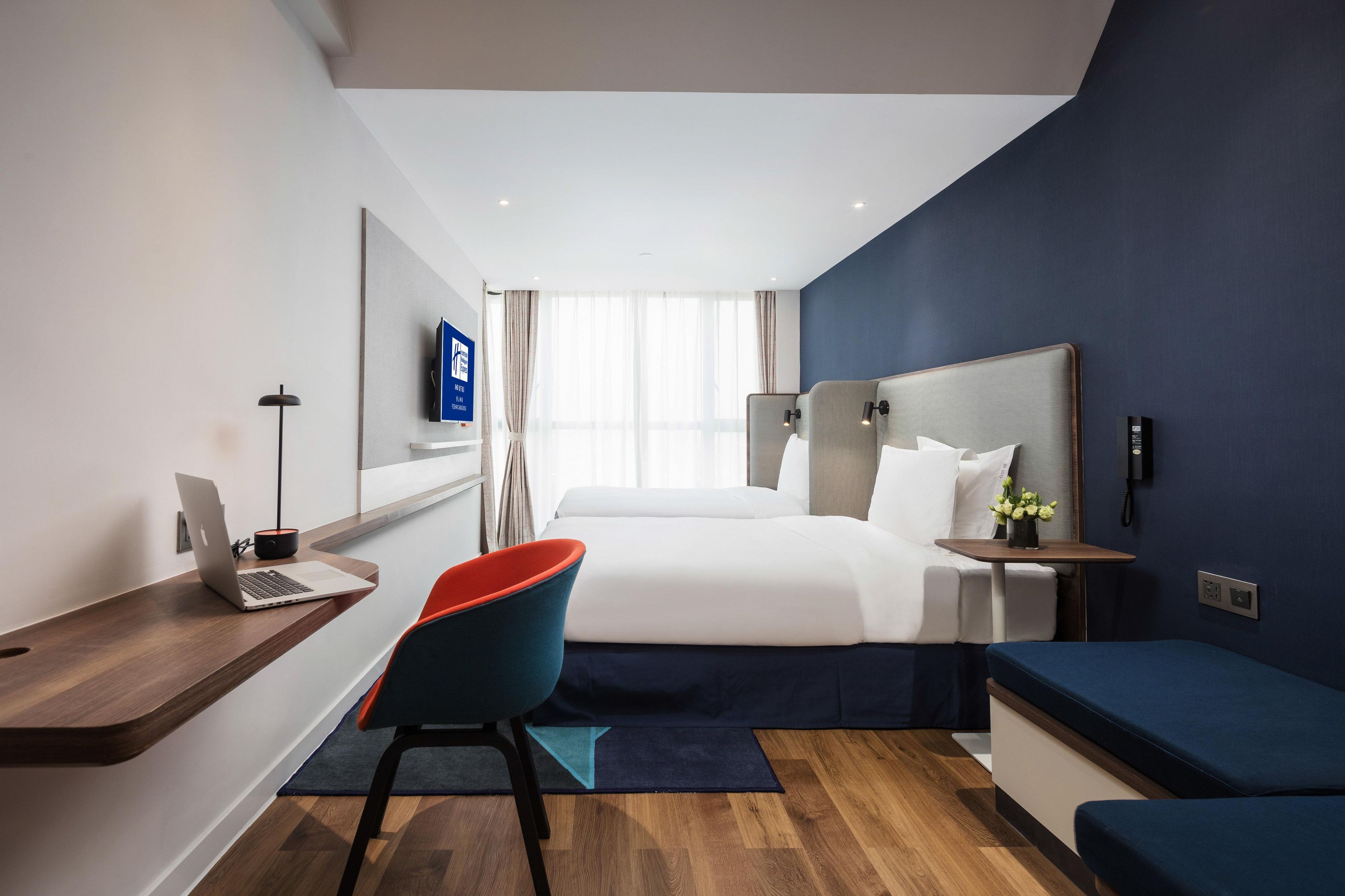 Una habitación de hotel moderna con una cama, escritorio, silla y una pequeña mesa con un florero.