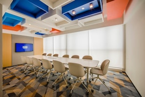 Une salle de conférence avec une longue table, des chaises, un téléviseur à écran plat et une moquette à motifs.