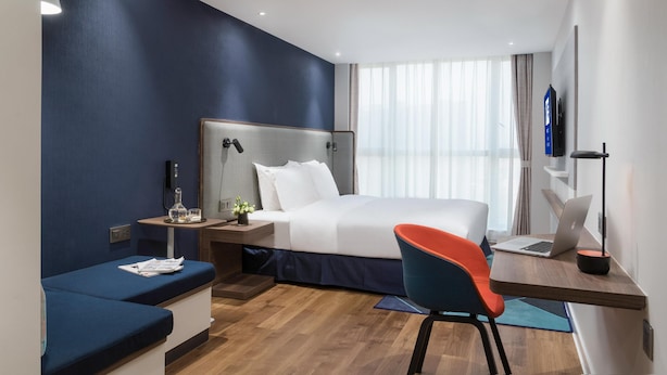 A modern hotel room with a bed, a desk with a laptop, a chair, and a small table with a lamp. - Holiday Inn Express Foshan Chancheng (Foshan)