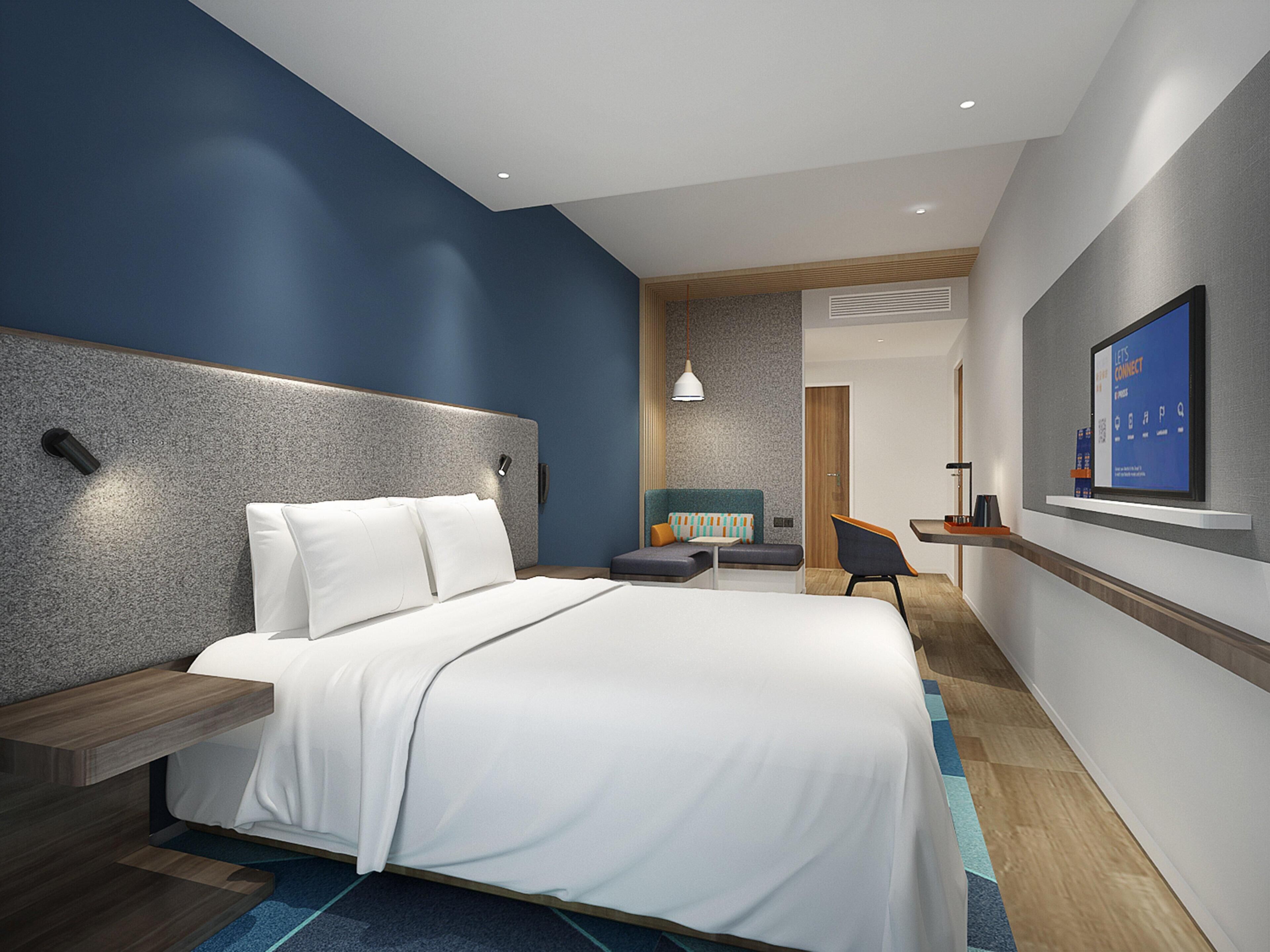 A modern hotel room with a large bed, a desk, a chair, and a TV mounted on the wall.