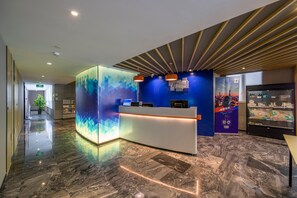 Zona de recepción de hotel con diseño moderno, una mesa de recepción y una vitrina de vidrio.
