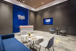 A modern hotel lobby with a reception desk, seating area, and a TV screen displaying hotel information.
