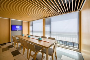 Un salón de conferencias con una mesa larga, sillas, una televisión y ventanas amplias con vistas.