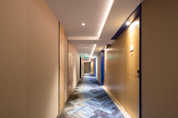 Pasillo de hotel con alfombra estampada, puertas a ambos lados e iluminación empotrada.