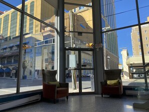 Un vestíbulo de hotel con ventanas amplias, dos sillones y una puerta de cristal.