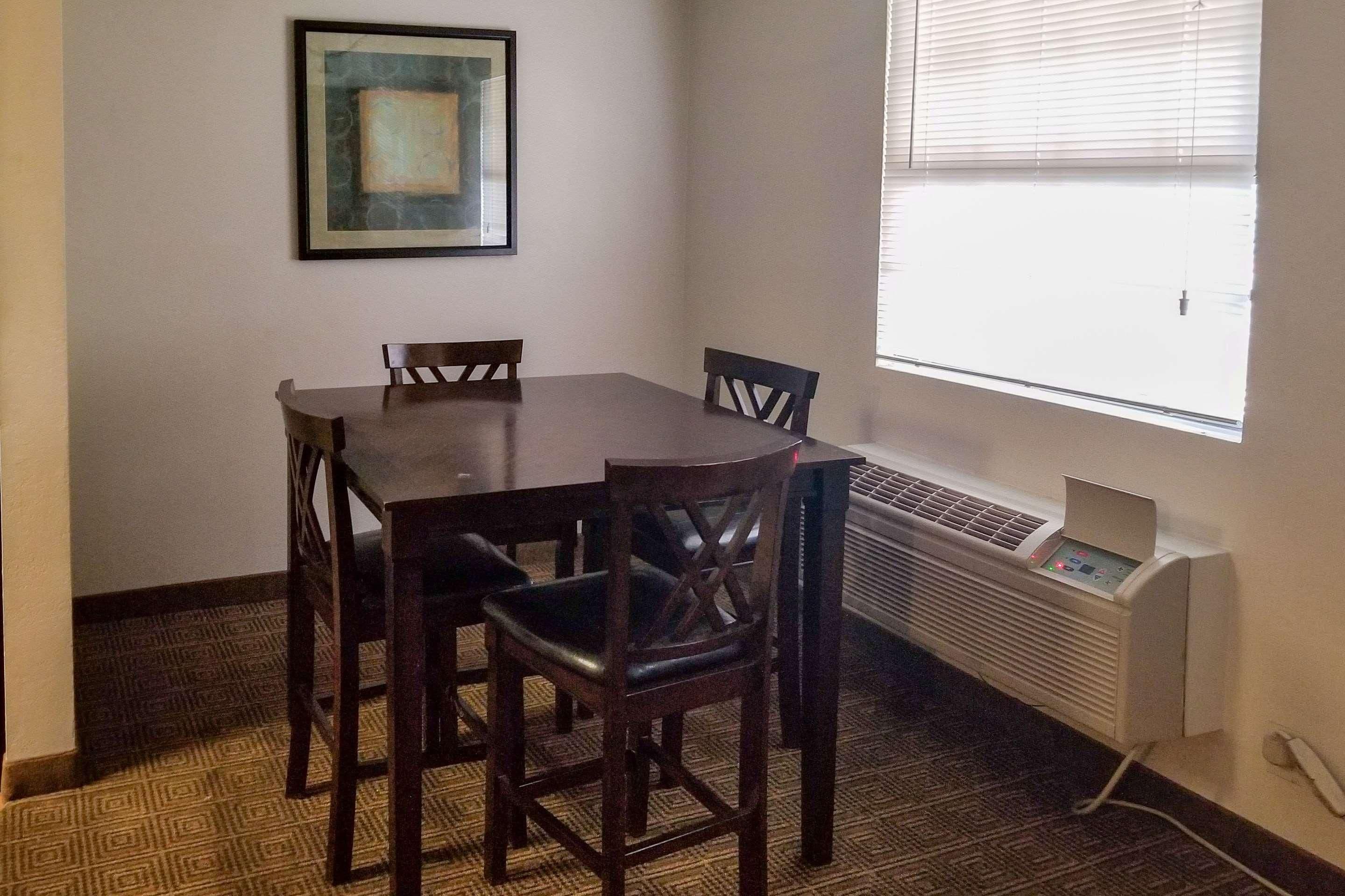 A dining area with a table and chairs, a framed picture on the wall, and a window with blinds.
