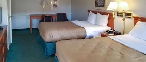 A hotel room with two beds, a desk, a chair, a lamp, and a painting on the wall.