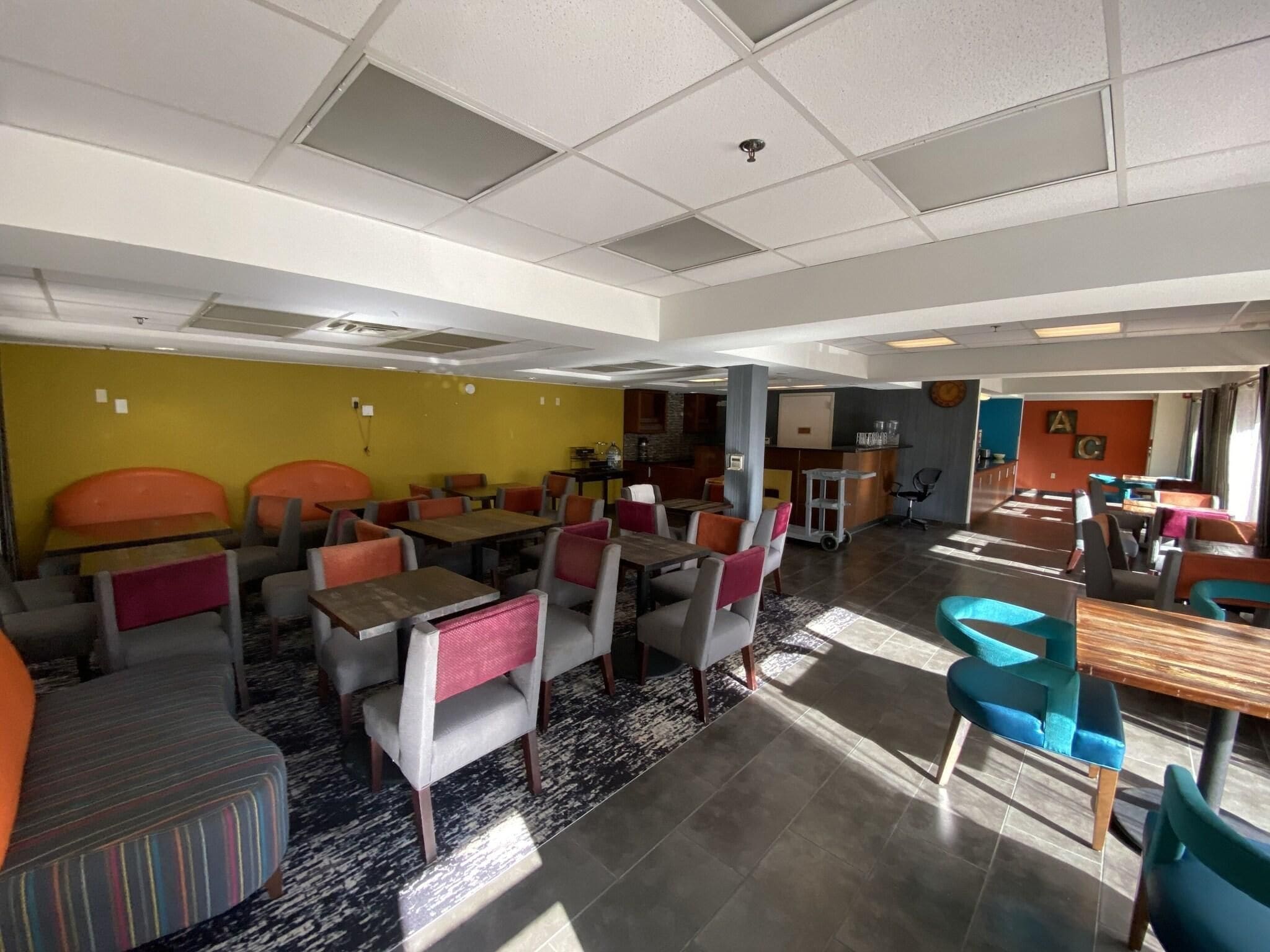 A spacious dining area with multiple tables and chairs, a kitchen in the background, and a yellow accent wall.