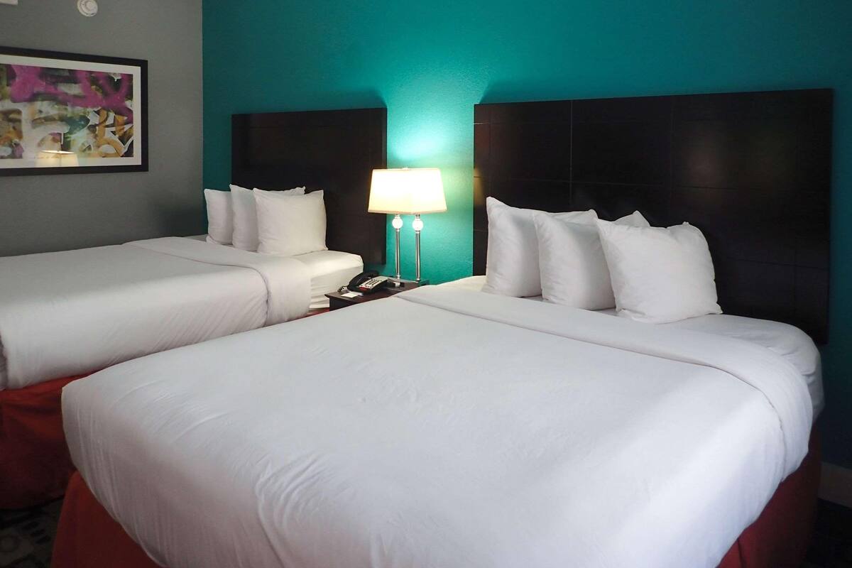 Camera d'albergo con due letti, un comodino con lampada e un quadro appeso al muro.