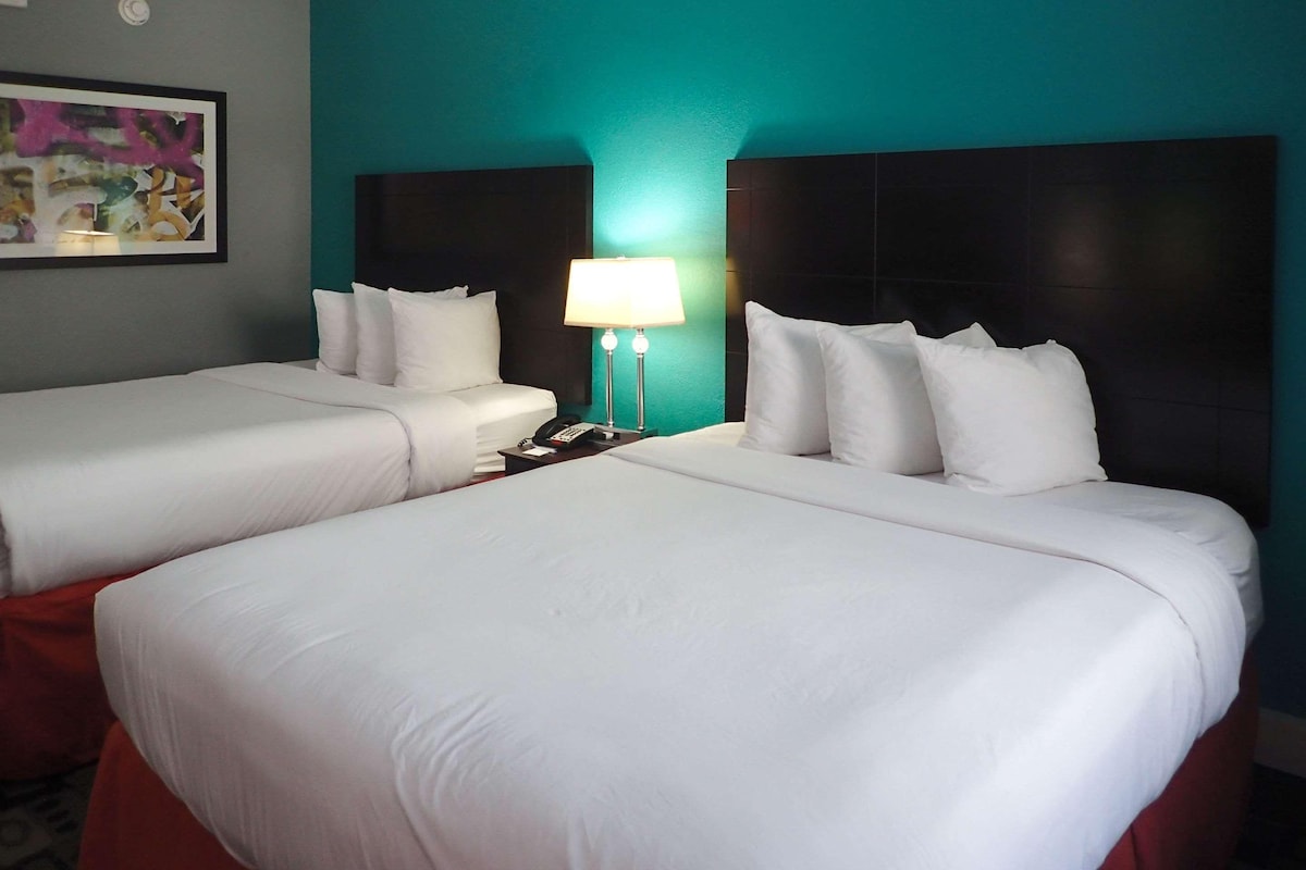 A hotel room with two beds, a nightstand with a lamp, and a painting on the wall.