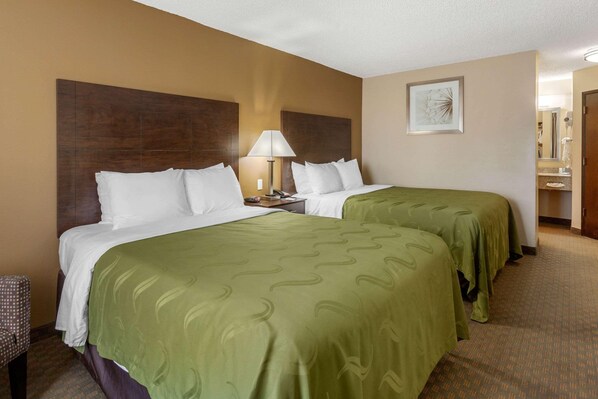A hotel room with two beds, a nightstand, a lamp, a chair, and a bathroom visible through an open door. - Quality Inn (Ontario)