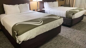 Two double beds with white linens, a nightstand with a lamp, and a carpeted floor. - Quality Inn (Ontario)