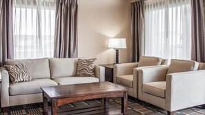 A hotel room with a sofa, armchairs, a coffee table, a lamp, and sheer curtains. - Quality Inn (Ontario)