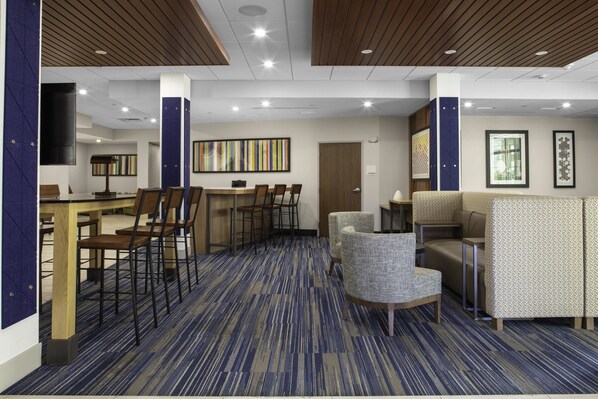A modern hotel lobby with a blue carpet, wooden ceiling panels, a dining area with chairs, and a seating area with upholstered chairs. - Holiday Inn Express Wells-Ogunquit-Kennebunk by IHG (Wells)
