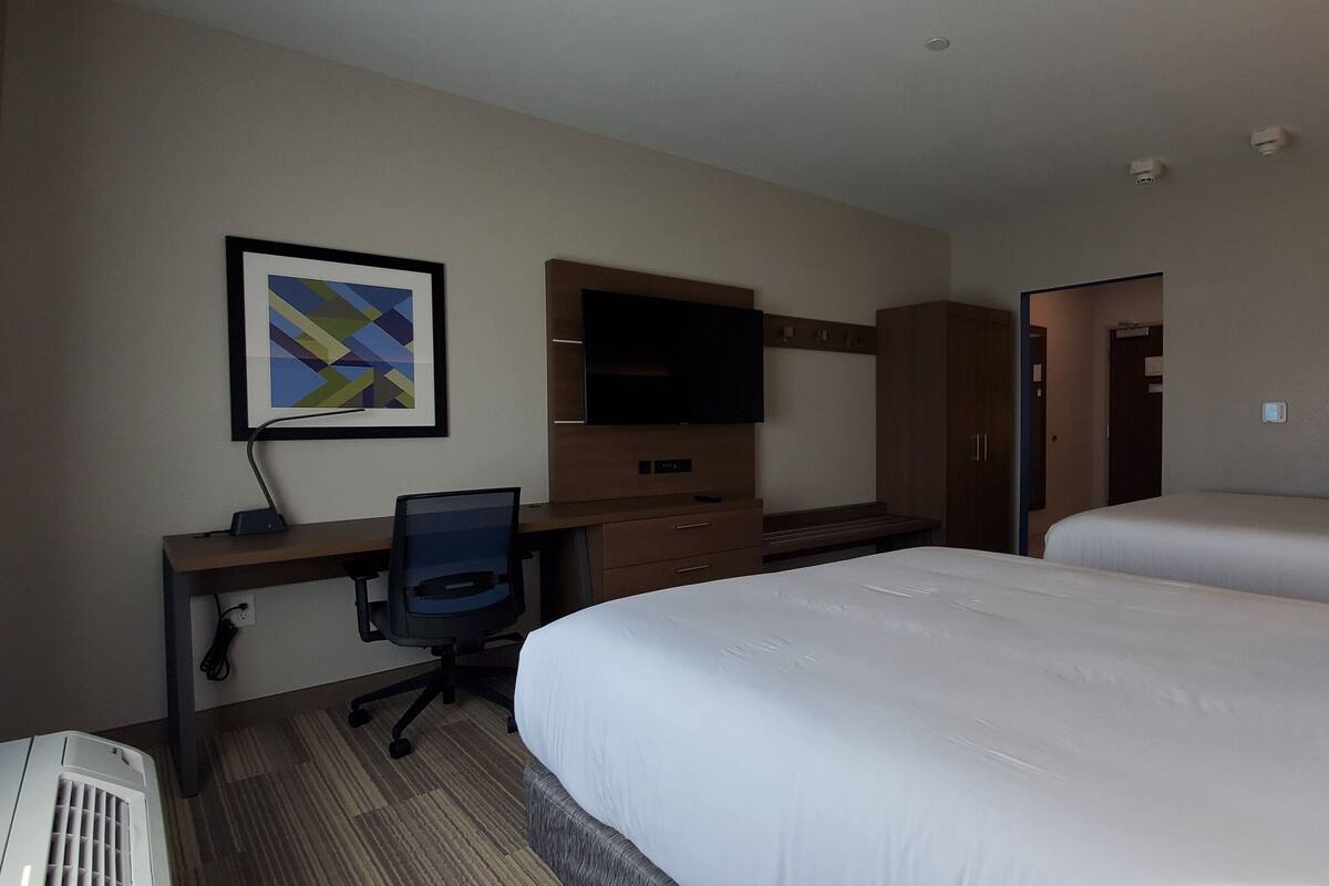 A hotel room with a bed, a desk with a chair, a flat-screen TV, and a wardrobe.