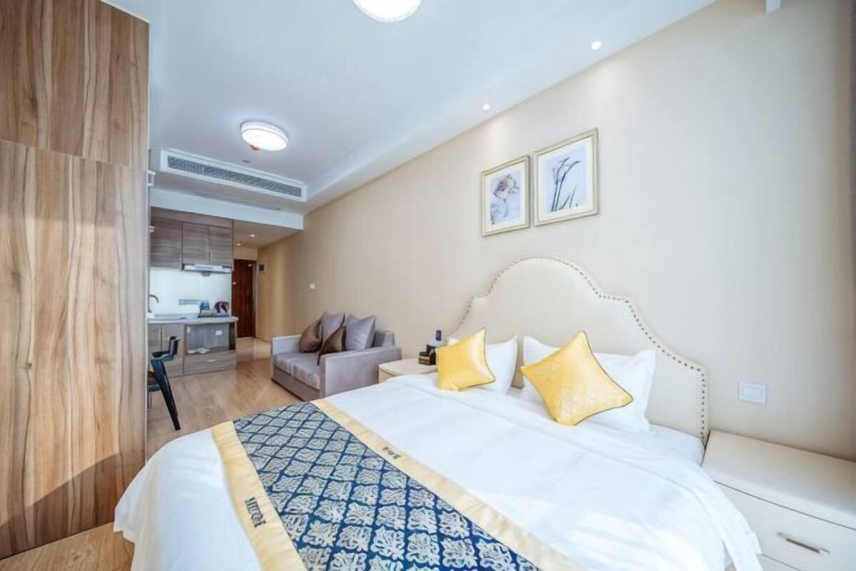 A hotel room with a bed, bedside table, and a view of the kitchen area.