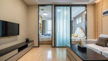 A modern hotel room with a flat-screen TV, a sofa, a bedside table, and a sliding door leading to a bathroom.