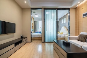 Una habitación de hotel moderna con televisor de pantalla plana, un sofá, una mesita de noche y una puerta corredera que da al baño.