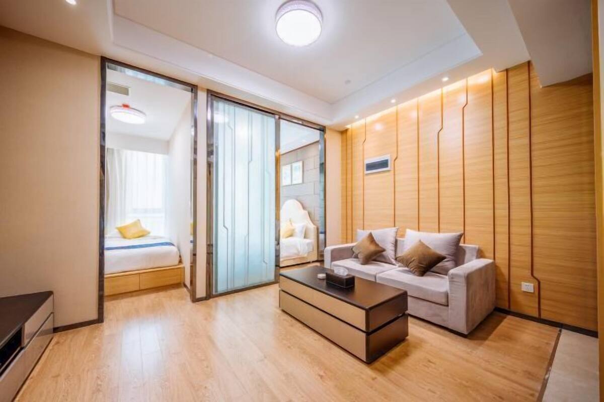 A modern hotel room with a bed, a sofa, a coffee table, and a sliding door leading to another room.