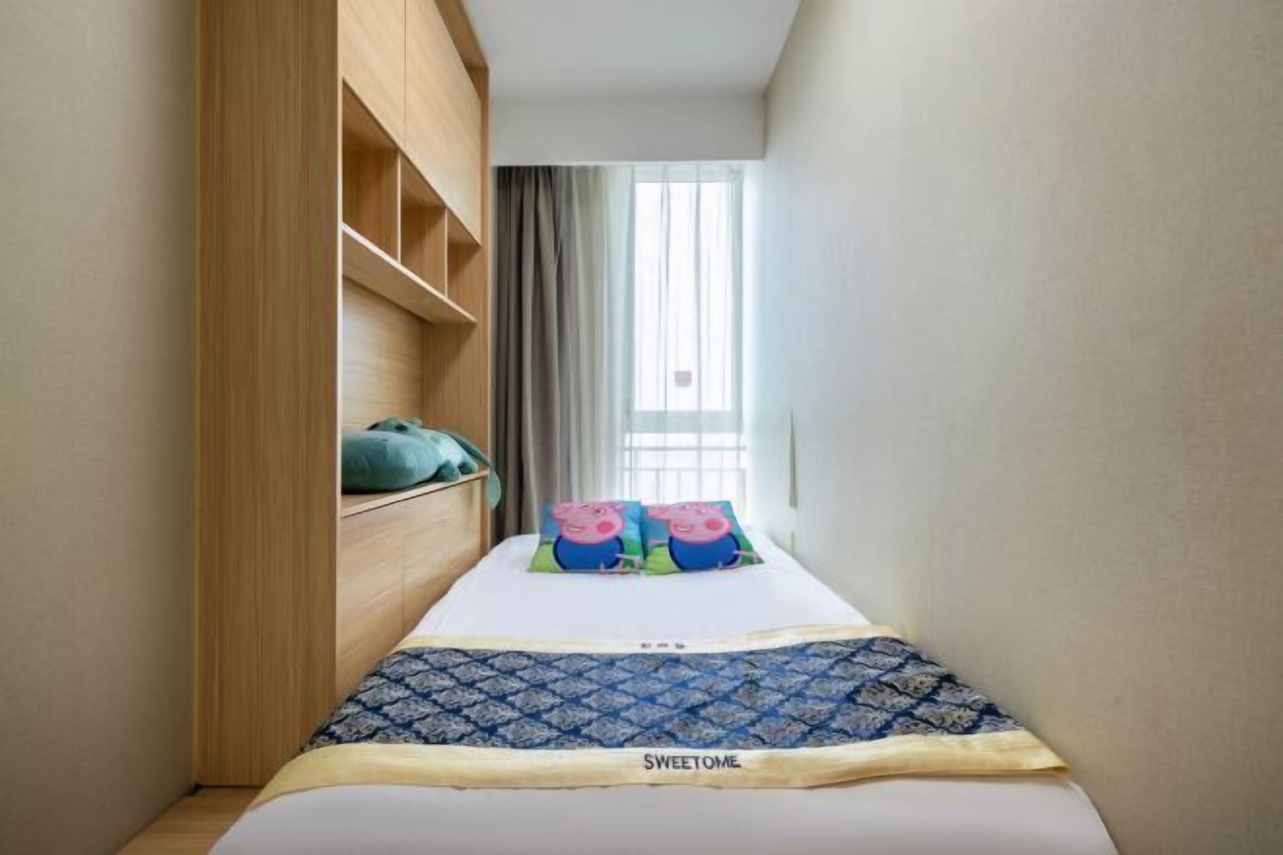 A narrow room with a bed, a wooden wardrobe, and a window with curtains.