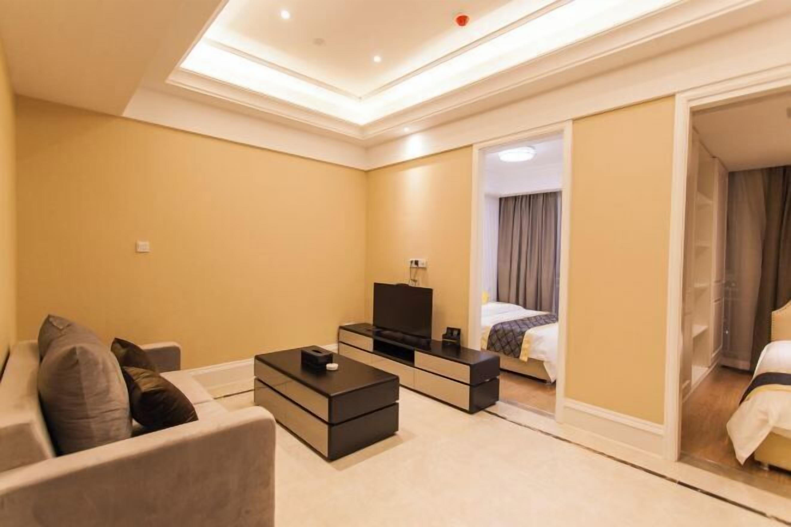 Quarto de hotel com sofá, televisão, mesa de cabeceira e cama.