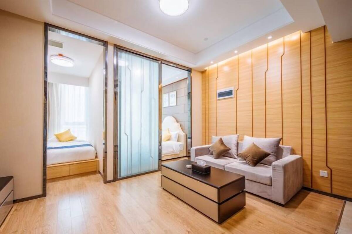 A modern hotel room with a sliding door, a sofa, a coffee table, and a wooden accent wall.