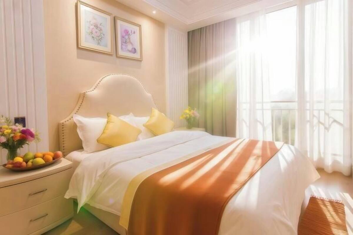 A hotel room with a bed, a nightstand with a vase of flowers, and a window with curtains.