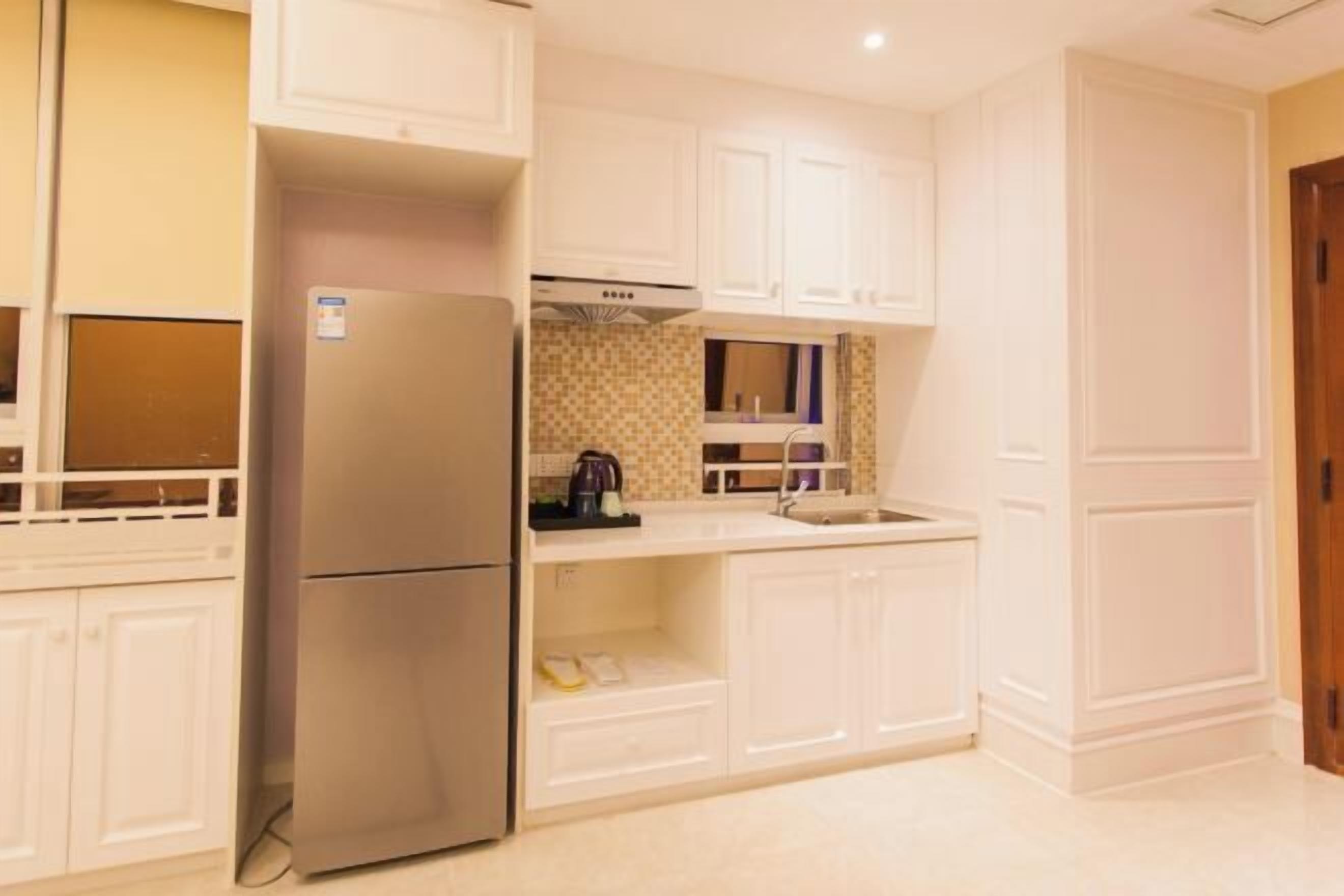 A compact kitchen with white cabinetry, a stainless steel refrigerator, and a tiled backsplash.