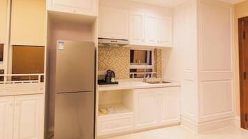 A compact kitchen with white cabinetry, a stainless steel refrigerator, and a tiled backsplash.