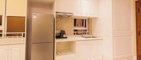 A compact kitchen with white cabinetry, a stainless steel refrigerator, and a tiled backsplash.