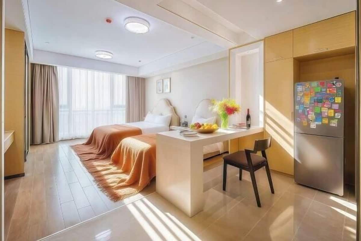 A hotel room with a bed, a desk with a chair, a refrigerator, and a window with curtains.