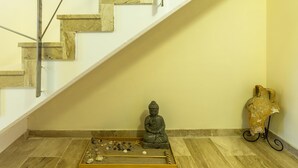 Una escalera con peldaños de mármol y barandillas de metal, una estatua de Buda, y un arreglo decorativo de conchas marinas y estrellas de mar en el suelo.