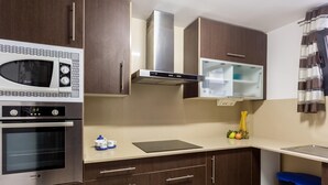 Una cocina moderna con microondas, horno y campana extractora de acero inoxidable. Hay armarios de madera, una encimera y un cubo de basura.