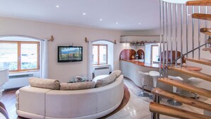 Ein modernes Wohnzimmer mit einem gebogenen weißen Sofa, einem an der Wand montierten Fernseher und einer Holztreppe.