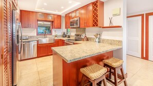 A modern kitchen with wooden cabinets, stainless steel appliances, granite countertops, and a central island with bar stools.