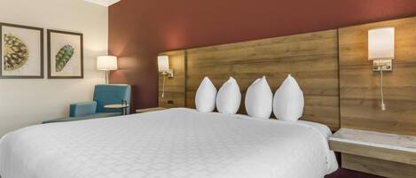 A hotel room with a large bed, a wooden headboard, wall-mounted lights, a small round table, and two framed cactus artworks.
