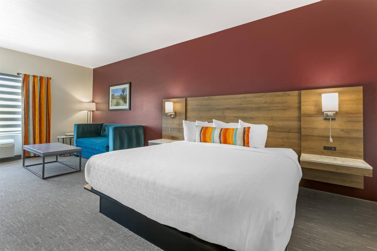 A hotel room with a large bed, a desk, a chair, and a nightstand.