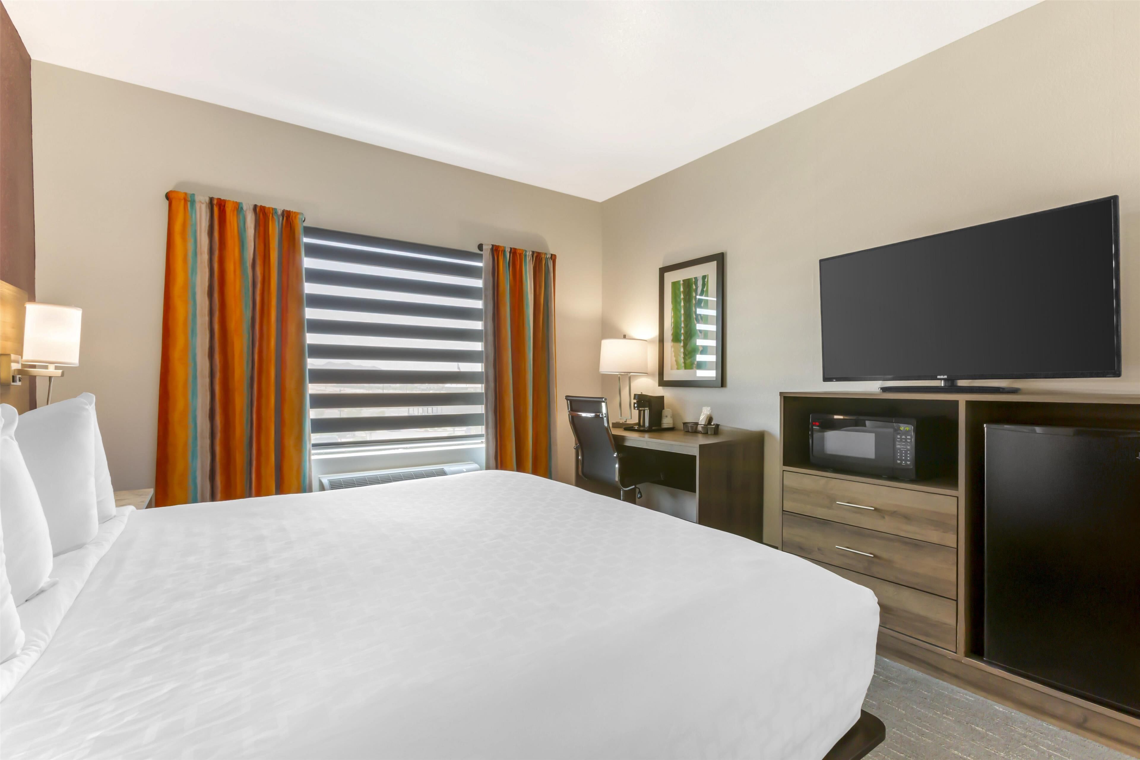 Quarto de hotel com uma cama grande, uma escrivaninha com cadeira, televisão, micro-ondas e frigorífico.
