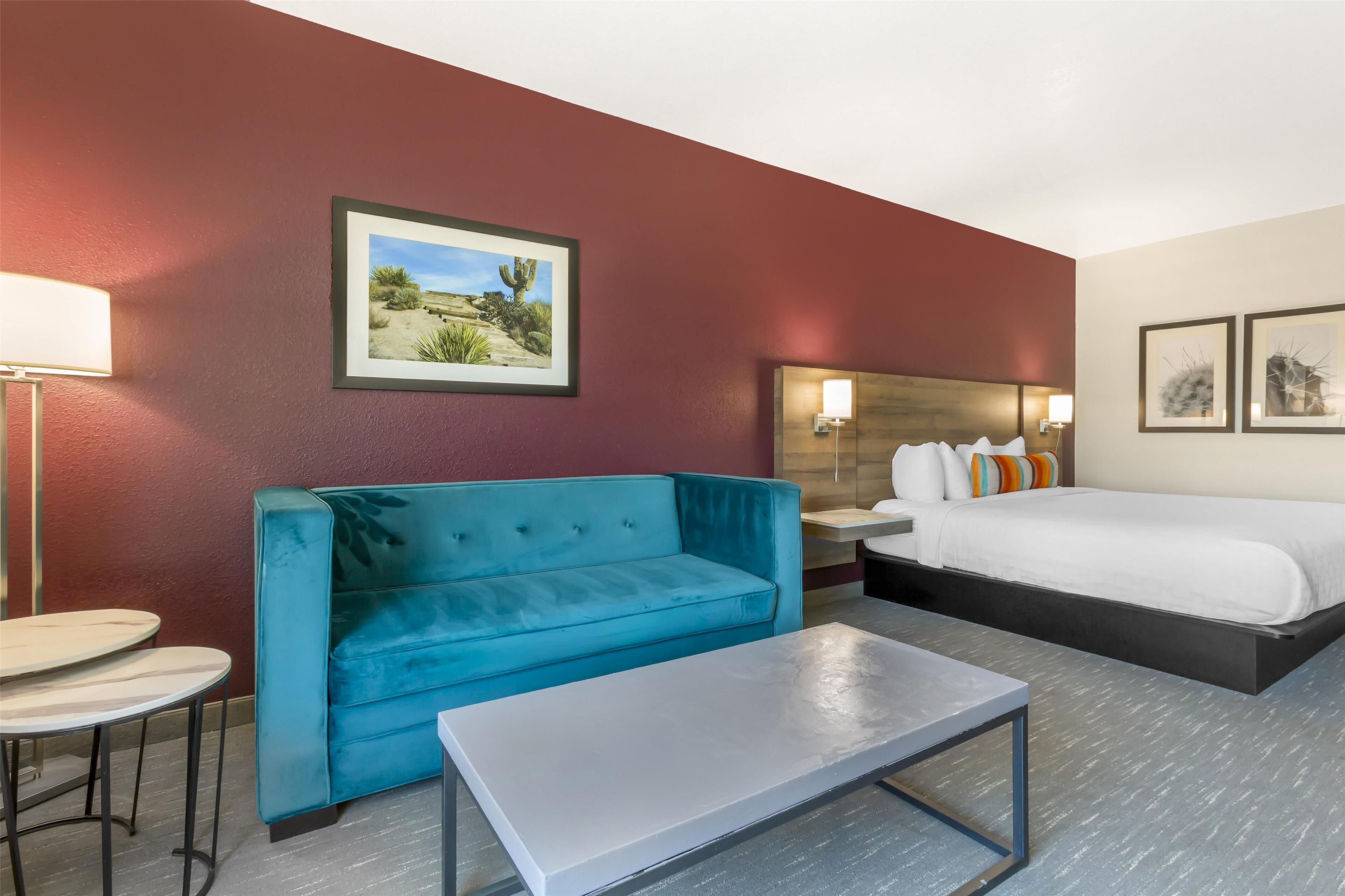 A hotel room with a blue sofa, a single bed, a small table, and a framed picture on the wall.