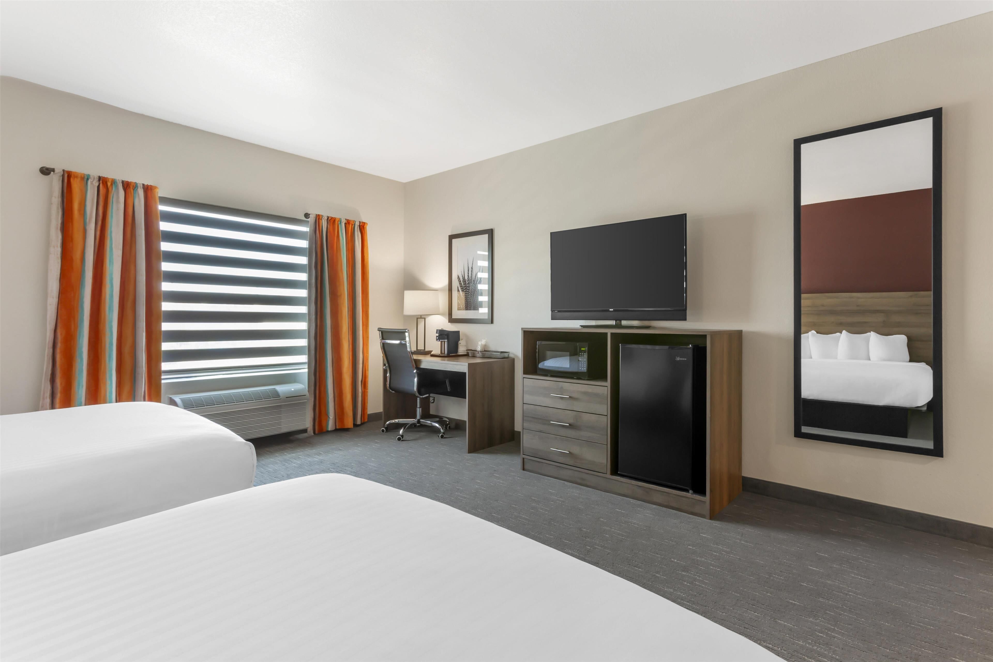 A hotel room with two beds, a desk with a computer, a TV, and a minibar.