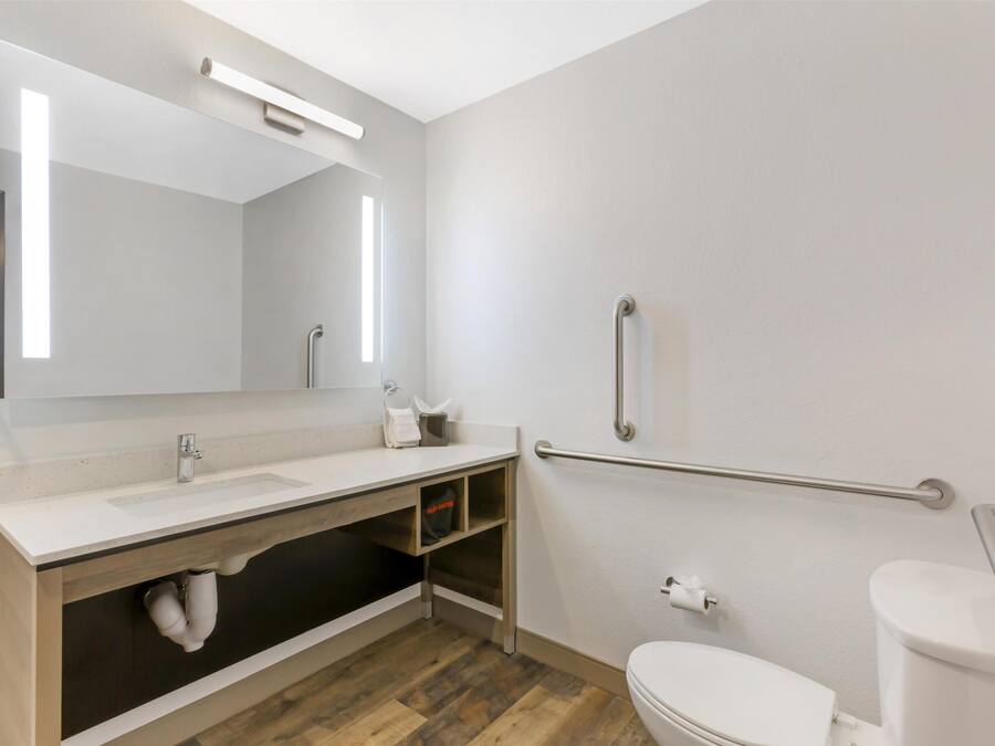 Een moderne badkamer met een witte wastafel, spiegel en toilet. Er is een wastafelmeubel met opbergruimte en een handgreep voor toegankelijkheid.