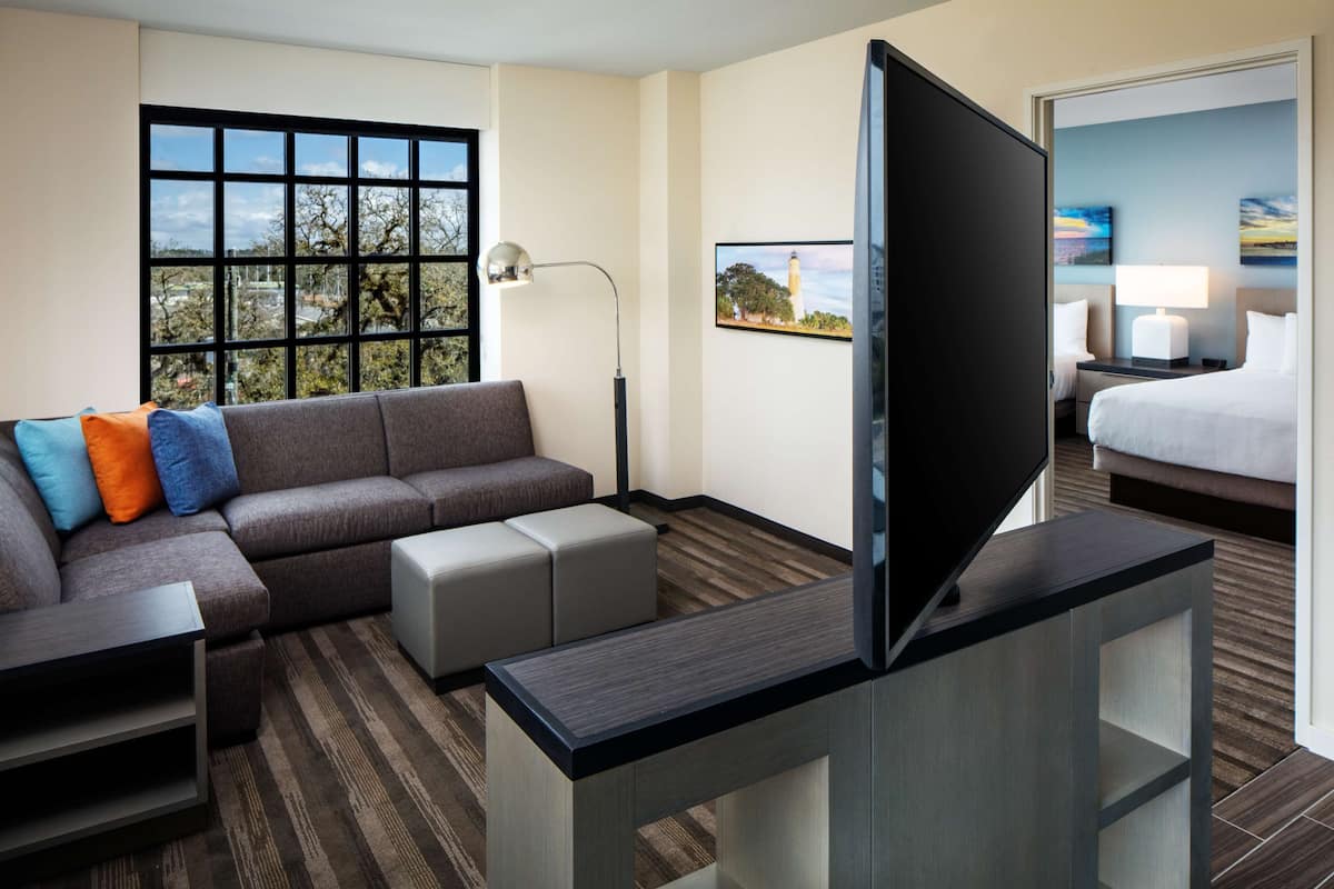 Una habitación de hotel con sofá, televisión, escritorio, lámpara y cama.
