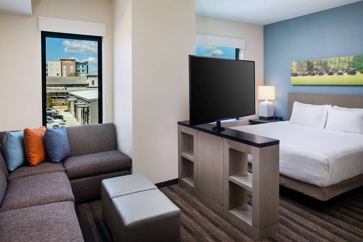 Habitación de hotel con una cama grande, un sofá, un televisor y una ventana con vistas a edificios.